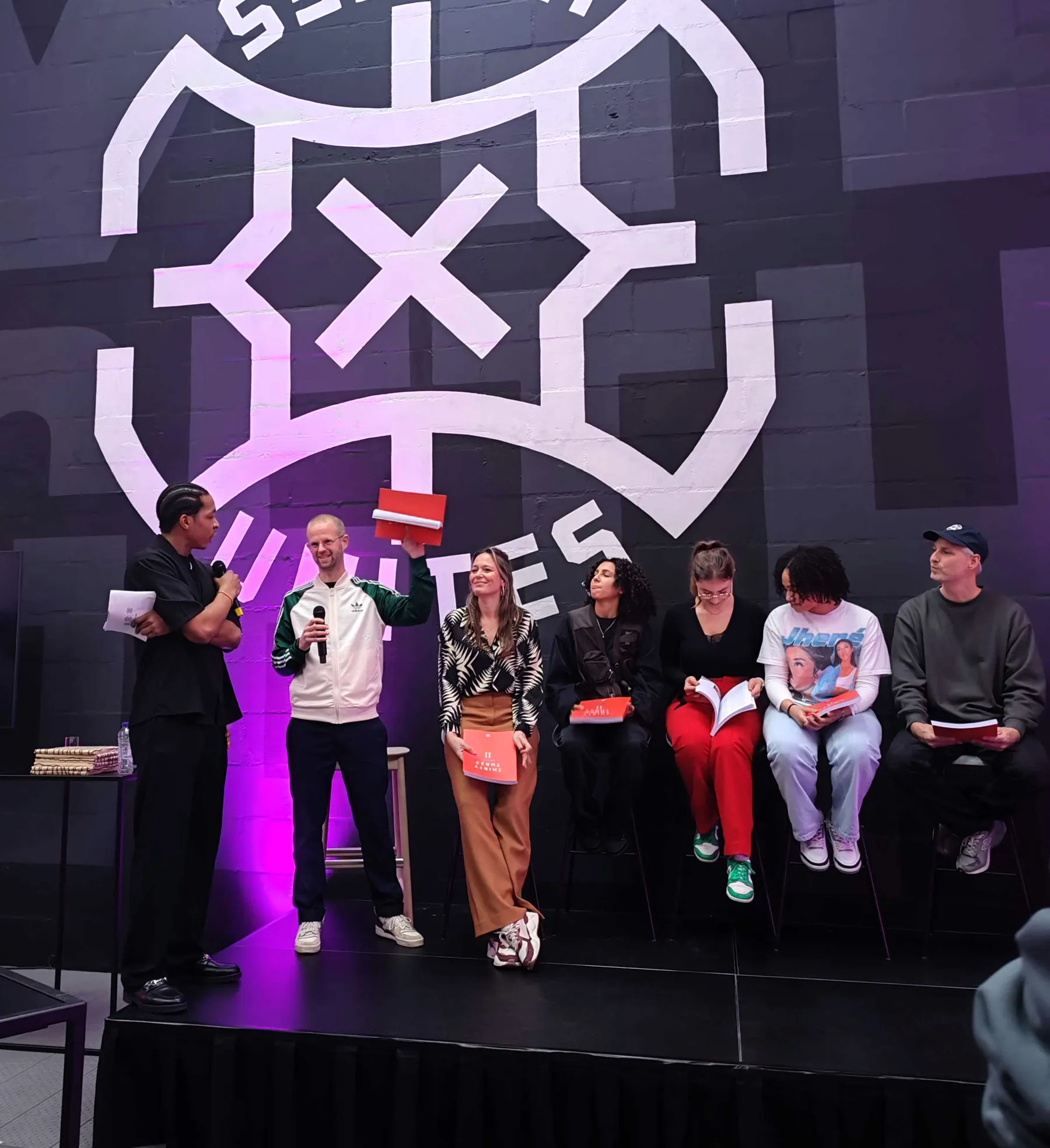 presentatie op een podium voor het logo van 3X3 Unites, een man houdt een rood boek omhoog
