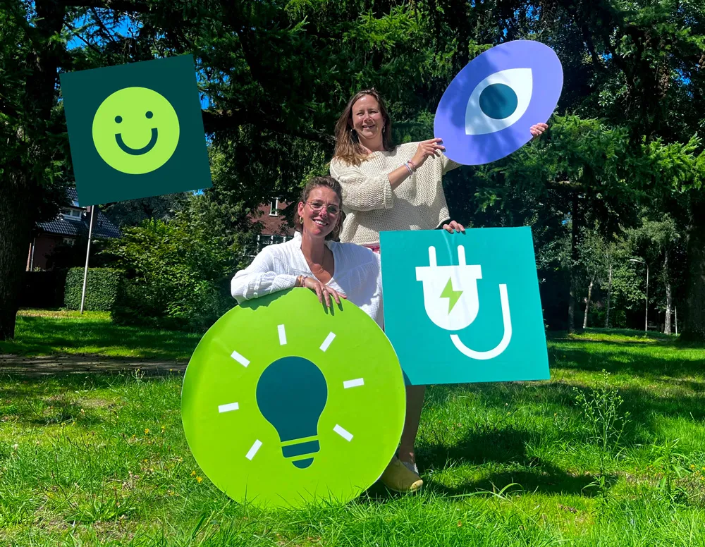 twee vrouwen die grote illustraties vasthouden van een oog, een stekker en een brandende lamp, en een blij smiley