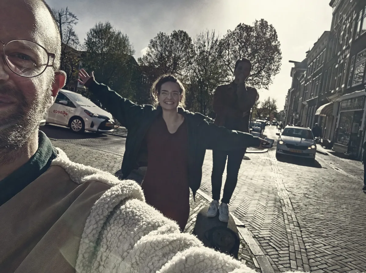 man maakt een selfie op straat in Utrecht, een vrouw erachter lacht met open armen