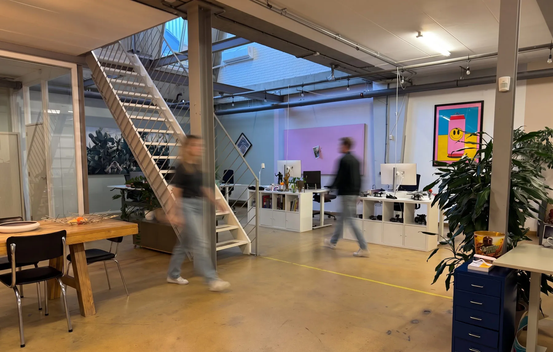 de studio met trap en bureaus, twee mensen lopen voorbij